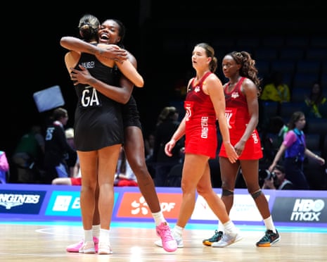Two New Zealand netball players embrace joyfully while two England players look on dejectedly