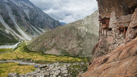 Wooden houses constructed in gaps in the rock face and below the settlement of Halji surrounded by peaks.