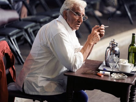 Bradley Cooper in the film Maestro, sitting at a table and smoking a cigarette