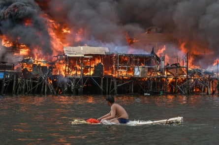 A man sitting on a raft in the water watches houses on fire at Tondo in Manila