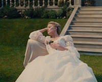 Margot Robbie as Cathy in a long-sleeved white wedding dress reclining on a lawn chair in front of a stone staircase