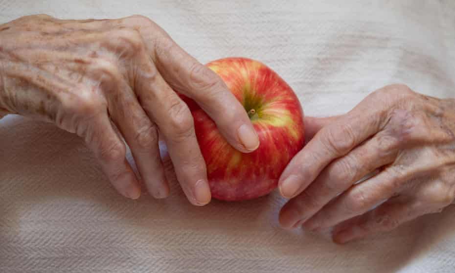 Elderly woman holding a ripe apple in her wrinkled hands against an off white background photographed from above.