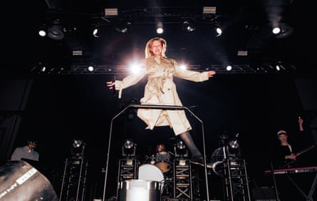 Hobert raised up from the stage with arms and legs wide and wearing a trenchcoat