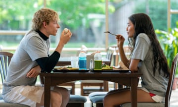 a young man and woman sit across from each other at a table, eating food