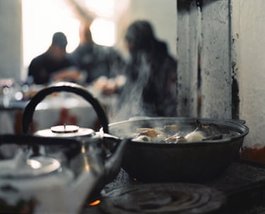 Dinner in Ruslan’s home, Ottuk, February, 2023 steaming pots on a hub with figures chatting in the background