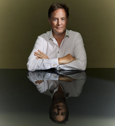 Nick Clegg sitting leaning on a tabletop, arms folded, in white shirt, against olive green background, July 2025