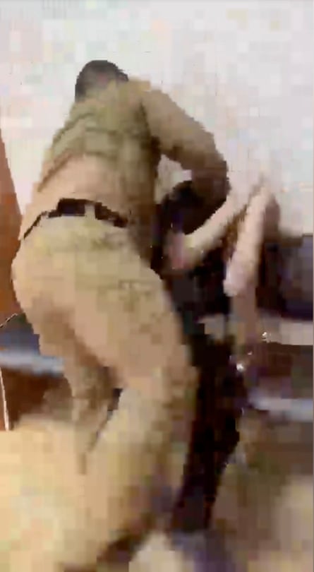 A rear-view image of an individual in combat fatigues beating a man sitting on a bench.