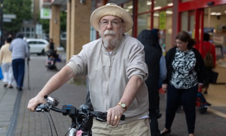 Arthur Farrow, in a frayed straw hat, jacket with sleeves pushed up, glasses and a beard, holds his bike and looks serious