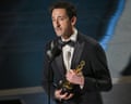a man in a tuxedo holds a trophy as he speaks into a microphone