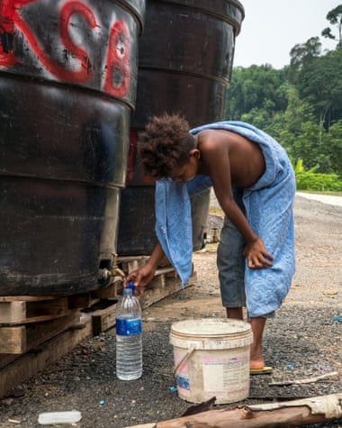 Boy in blue sarong fills bottle from graffitied tank.
