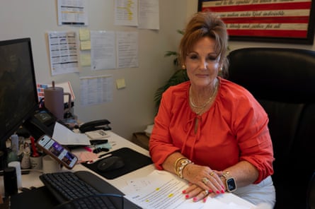 A woman wearing an orange blouse poses at her office desk