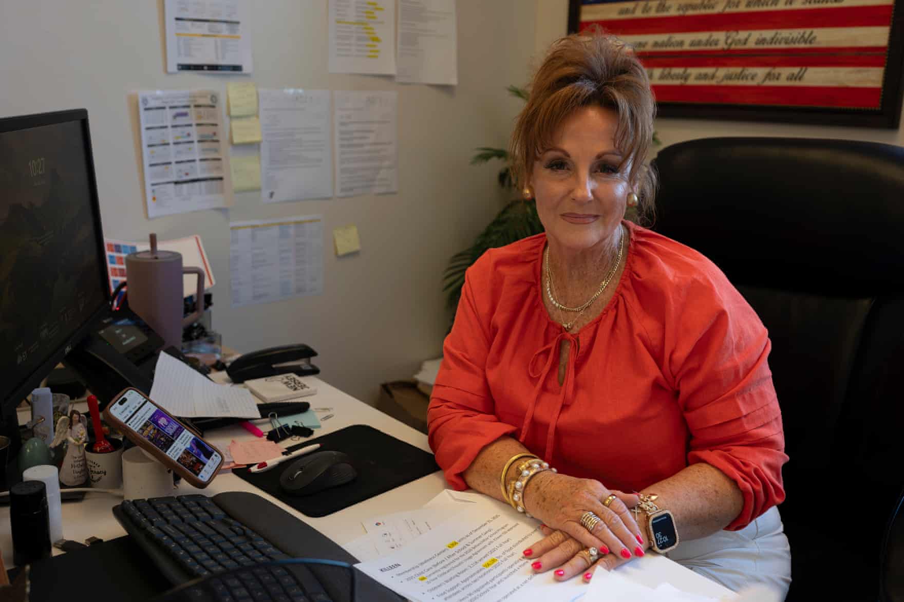 A woman wearing an orange blouse poses at her office desk