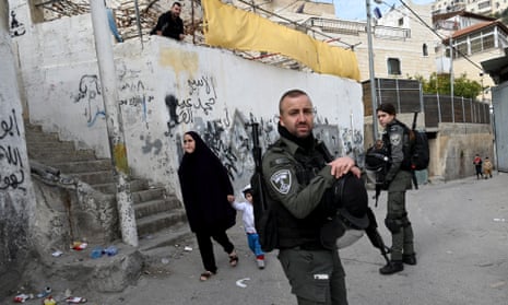 A Palestinian woman and child walk near Israeli border police stationed outside the sealed family home of Alqam Khayri ,the gunmen who killed seven Israeli Jews in a shooting attack on Friday.