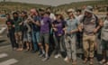 A group of activists link arms while standing on a road, as settlers stand behind them