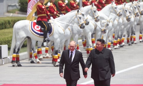 Putin (L) and Kim Jong Un (R) walk past a row of soldiers mounted on horses.