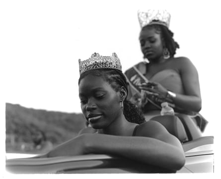 Two people in beauty pageant crowns and dresses look downwards