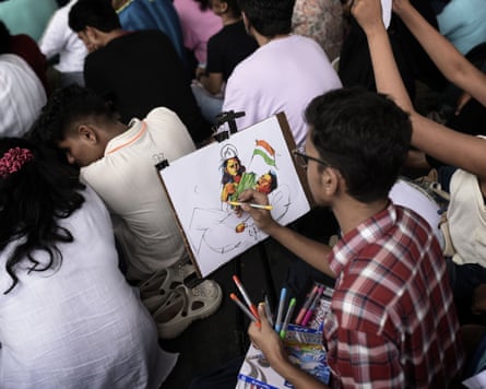 A protester draws a picture of the hunger striking protester lying down waving an Indian flag