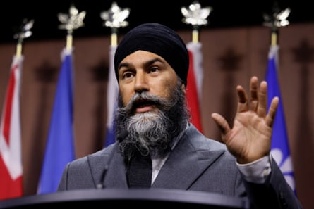 A man speaks at a podium with his hand raised, flags behind him