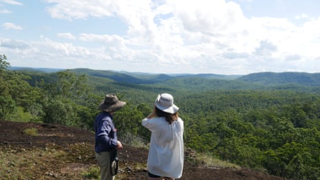 Two people in hats looking at forested hills