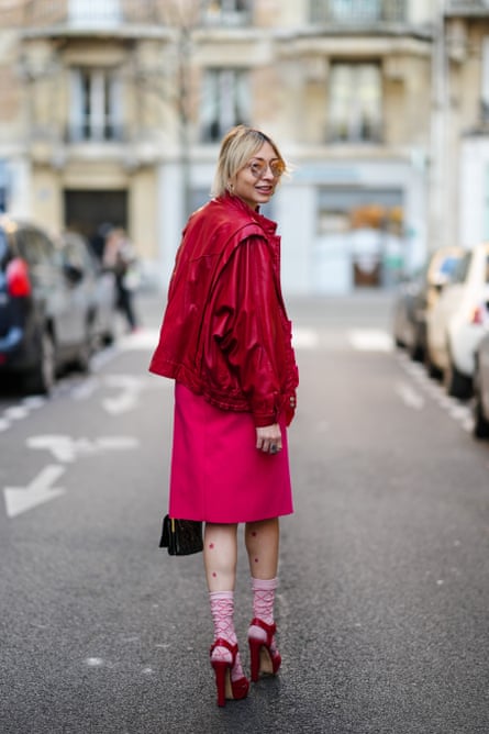 Backview of a woman walking down a Paris street, looking over her shoulder. She’s dressed in a fuchsia jacket, skirt and high heels.