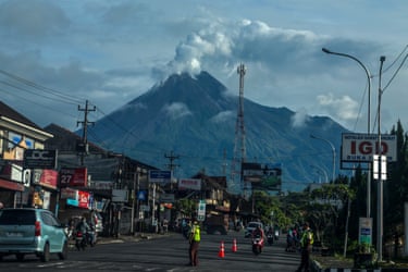 A cloud rising from Mount Merapi in the distance, seen from a road with cars and motorcycles