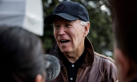 Older white man in black ball cap, leather jacket with collar turned up, with the heads of people and a fuzzy microphone large and blurry in the foreground.