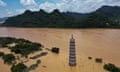A pagoda is seen from above half submerged in floodwater with a river burst from its banks and hills in the background.