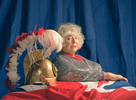 Portrait of Miriam Margolyes sitting at a table with a union flag tablecloth and a helmet to her left