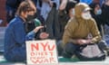 two people sit on the ground. one has a sign that says 'nyu divest from war'