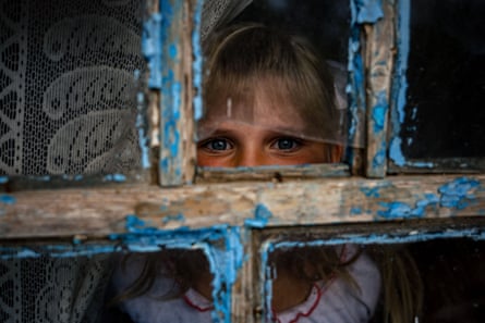 A child looks through a broken window.