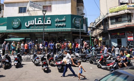 A man walks out of a bakery with a bag of subsidised flatbread, as others continue to wait in a queue, in the Lebanese capital Beirut on 29 July 2022.