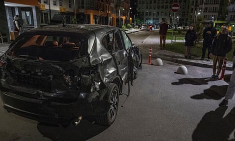Kyiv residents stand next to a car damaged by the remains of a drone.