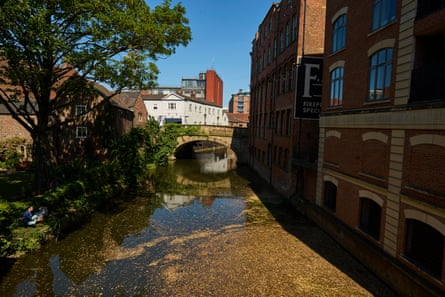 Um rio banhado pelo sol passa por prédios e por baixo de uma ponte.