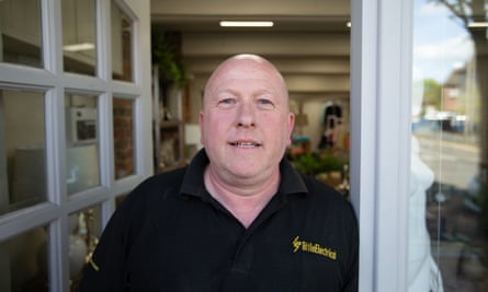 Ian Carson, 50; he wears a black polo shirt and stands in a doorway.