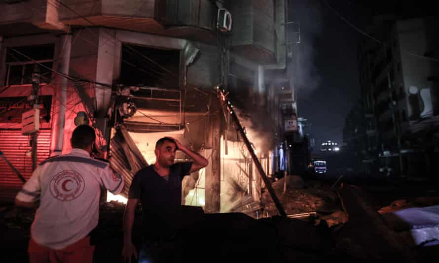 A Palestinian man looks on in disbelief as firefighters search urgently for survivors and bodies under rubble in Gaza City early on Sunday