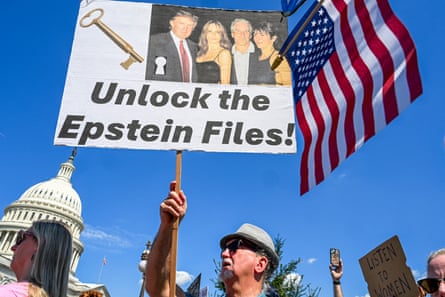 a person holds a sign that shows a key, a picture of two men and two women and the words ‘unlock the Epstein files’