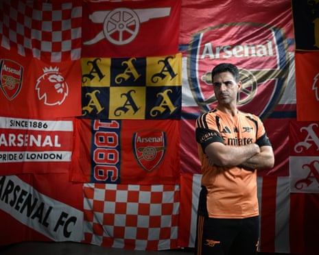 Mikel Arteta poses in front of an Arsenal banner