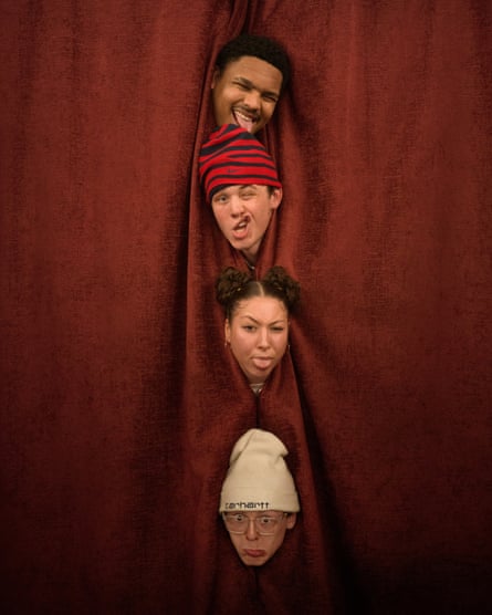 Four young people put their heads through the gap in a curtain, all on top of one another.