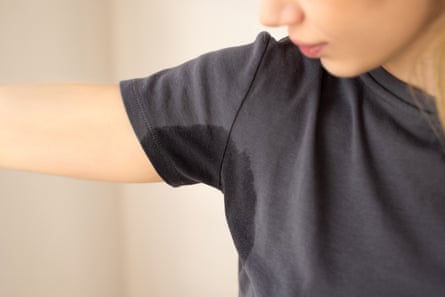 Close up of a part of a young woman's face to right of image looking at a patch of sweat showing under the left arm of her grey T-shirt