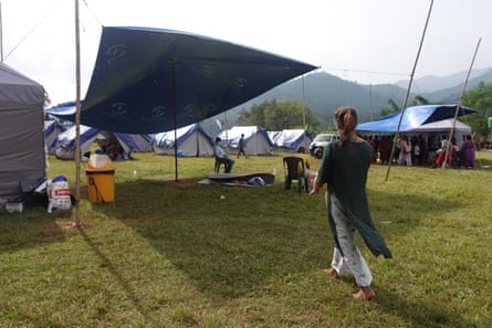 A woman holding her child walking away from the camera towards a makeshift tent shelter