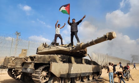 Palestinians hold a flag on top of a destroyed Israeli tank.