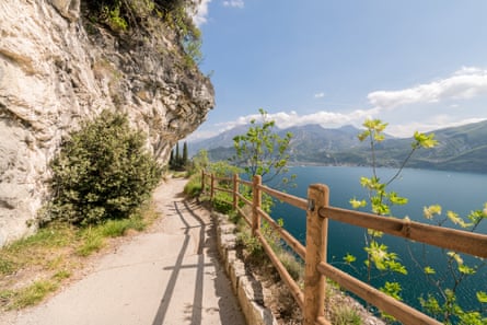 Path with overhanging rock/cliff with wooden fence and lake. Distant mountains