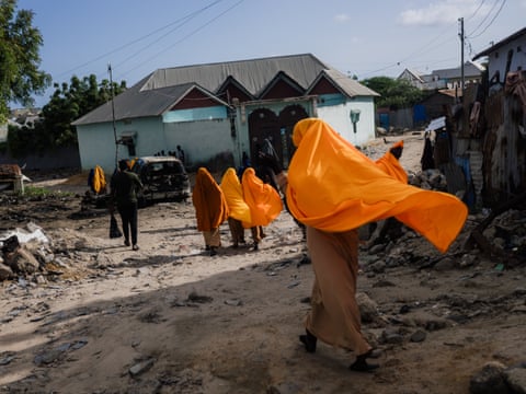 In Kismayo, people in vivid orange headscarves walk along a rubble-strewn dirt street