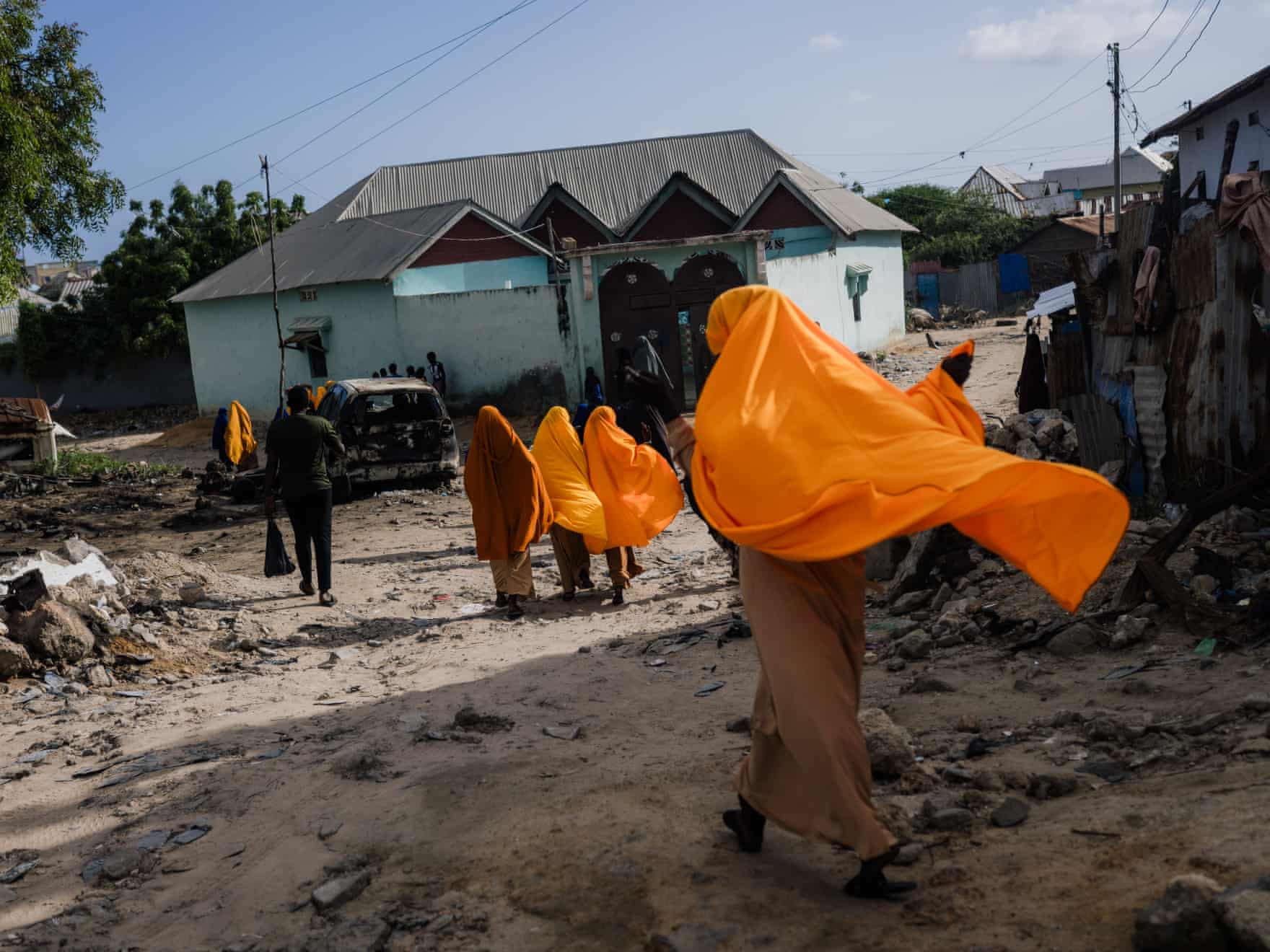 In Kismayo, people in vivid orange headscarves walk along a rubble-strewn dirt street