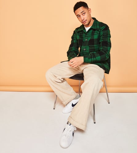 Coyle-Larner sitting on a chair in pale trousers, a green check shirt and white trainers