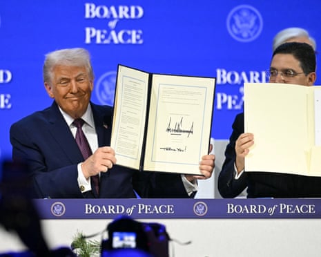 Donald Trump smiles while holding up a signed Board of Peace charter document