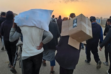 A Palestinian person carries an empty box of relief supplies from the Gaza Humanitarian Foundation, as displaced people walk near a food distribution centre in Rafah.