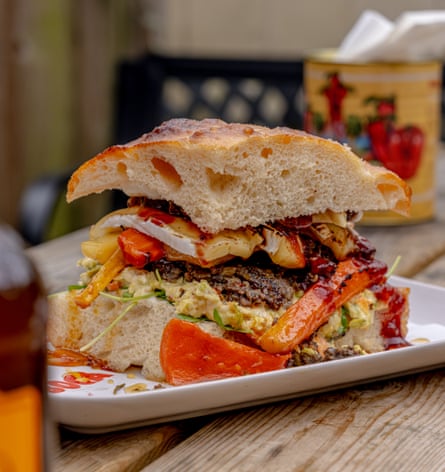 A tall sandwich stuffed with glazed vegetables and topped with thick slices of brie