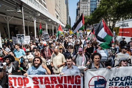 Mahmoud Khalil stands in the center of a row of people holding banners as they chant and lead a crowd of protesters