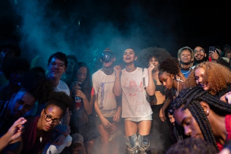 Vitória Jovem, wearing a mirrored visor, joins others cheering for friends competing during the Noite das Estrelas ball